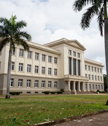 A wide-angle professional photograph of the Escola Superior de Guerra campus in Brazil, showcasing its grand neoclassical architecture and palm trees under a bright sky, symbolizing institutional stability and strategic thinking.
