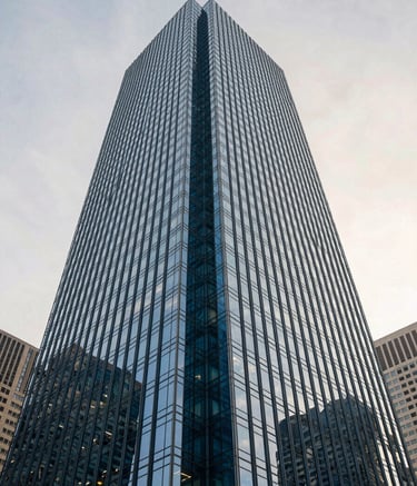 A wide-angle photography shot of a modern glass skyscraper in a North American city, reflecting a clear off-white sky, emphasizing corporate scale and professional media production with deep blue tones.