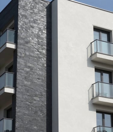 Architectural photography of a high-end residential building facade in Southern Europe featuring a clean, newly installed SATE thermal insulation system. The composition shows the contrast between a smooth, dark slate grey section and a light mist white finish. Bright, natural daylight highlights the professional texture of the material under a clear sky.