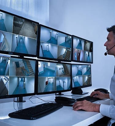 Security System Operator Looking At CCTV Footage At Desk
