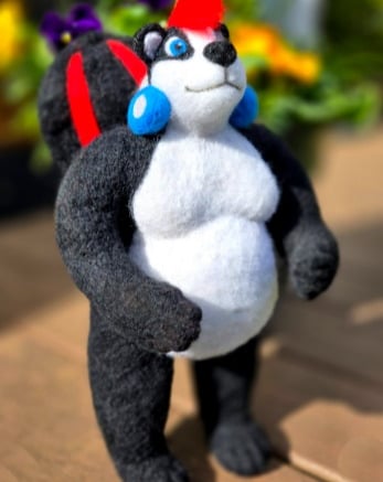 Handmade needle felted skunk figurine with a red mohawk and blue earrings standing outdoors.