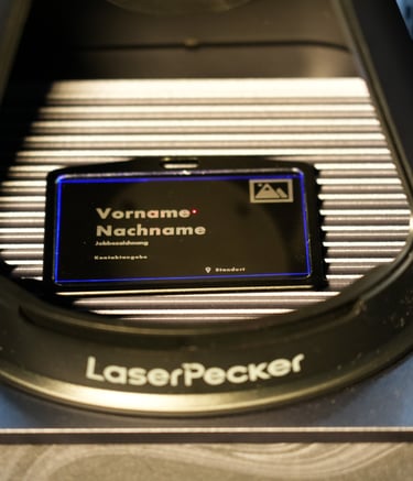 A LaserPecker engraving machine personalizing a black metal business card with custom text.