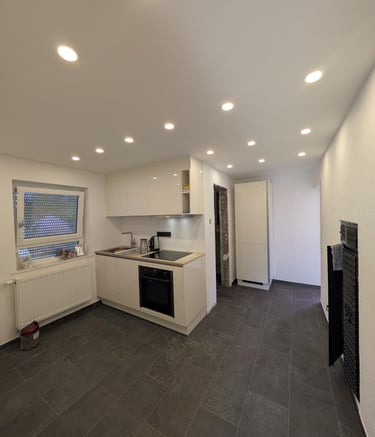 eine sanierte weiße Küche mit Deckenspots, grauen Fliesen auf dem Boden.