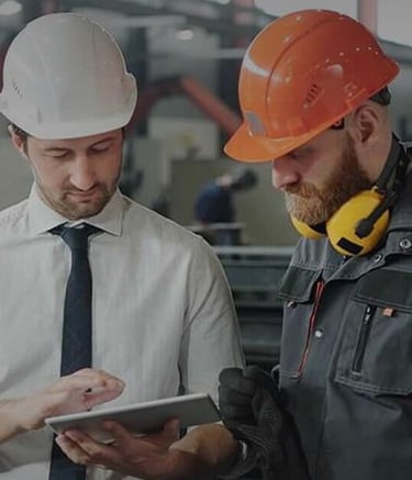 two men in hard hats and hard hats are looking at a tablet