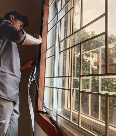 A washable velcro mosquito net being gently removed from a metal window frame for cleaning.