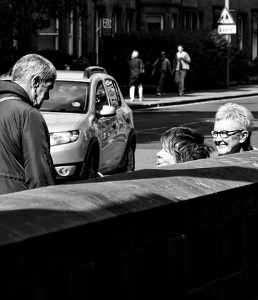 Three women, partially hidden behind a wall chat in the sunshine at Holy Corner, Edinburgh