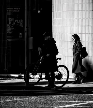 A woman on her bike, in shadow, and a woman behind her in the light at the bottom of Morningside Road, Edinburgh