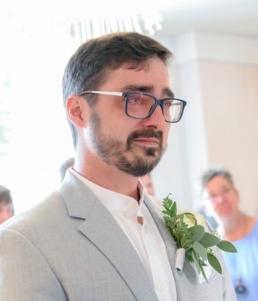 Emotionaler Bräutigam im hellgrauen Anzug mit Brille und Ansteckblume, der während der Trauung Tränen in den Augen hat.
