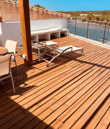 Luxury wooden rooftop terrace with lounge chairs and dining table overlooking a scenic river.