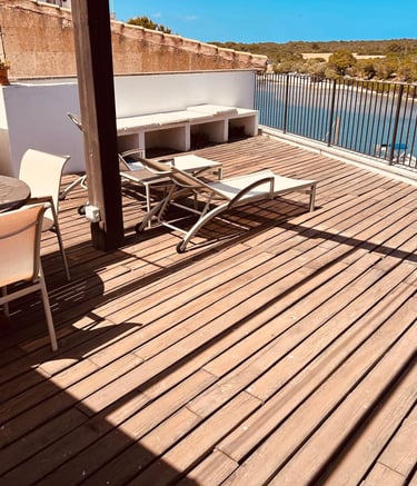 Luxury wooden deck terrace with lounge chairs and dining table overlooking a scenic river bay.