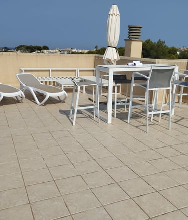 Modern rooftop terrace featuring white outdoor furniture, sun loungers, and a dining table with a sea view.