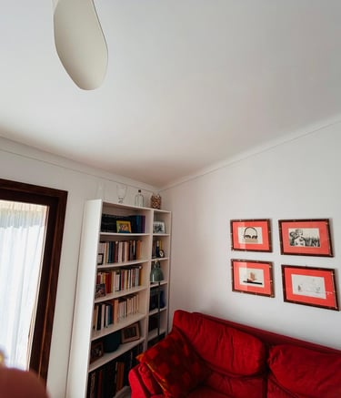Red sofa and white bookshelf in a bright living room with framed wall art.