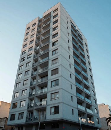 An wide-angle architectural shot of a contemporary apartment building facade in Venâncio Aires, RS, Brazil. The design is sleek with light blue and grey tones under a clear sky. South American / Brazilian urban environment.