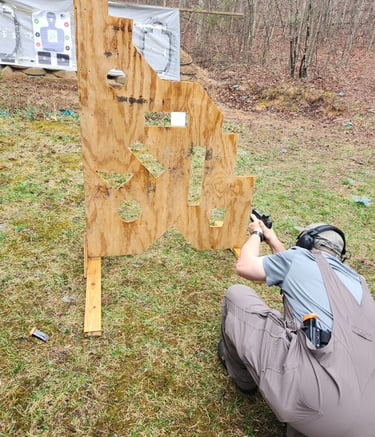 Kneeling man engaging targets from a barrier using self-defense firearm during training.