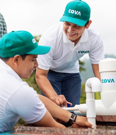 Two male workers with COVA hats, working on a PVC pipe water system.