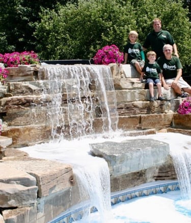 Leppek Landscape designed waterfall spilling into pool, surrounding landscaped patio.