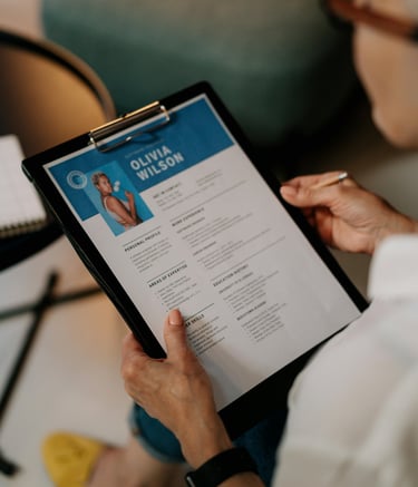 Main tenant un CV imprimé avec photo et nom visibles, sur une planchette à pince.