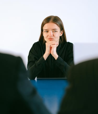 Jeune femme en entretien d'embauche face à des recruteurs, mains jointes sur la table.