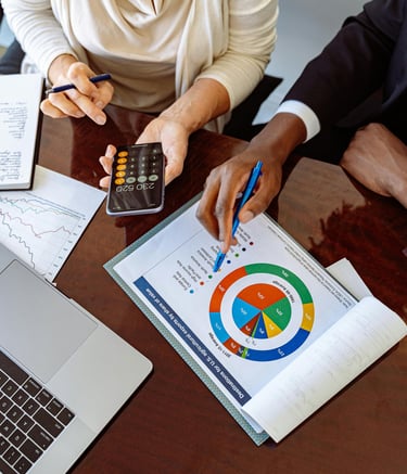 Mains de personnes en réunion pointant un graphique circulaire avec une calculatrice sur la table.