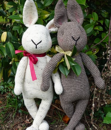 a couple of bunnies stuffed animals wearing a bow standing next to each other