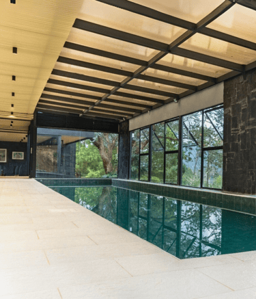 Piscina cubierta rodeada de ventanales, estructura metálica visible y cielo raso de madera.