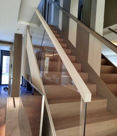 Modern interior staircase featuring light wood steps and a minimalist glass railing with white handrails.