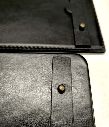 Close-up of a premium black leather tablet case with a brass stud closure and stitching details.