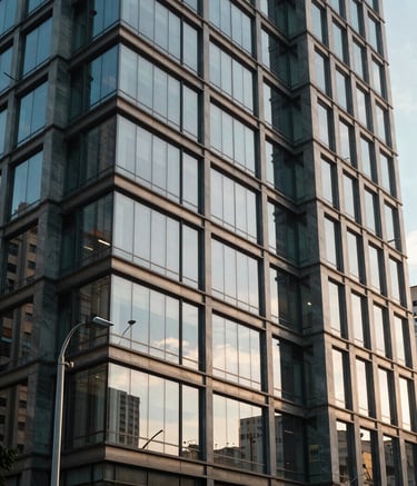 A sharp, professional photography shot of a sleek, contemporary commercial building facade with glass and steel elements, located in a South American / Brazilian business district. The lighting is crisp afternoon sun, reflecting off the building's surfaces in shades of soft blue and grey.