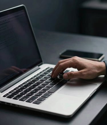 A close-up of a professional workstation with a sleek laptop. A person is typing efficiently. The setting is clean and modern with dark navy and cool grey tones in the background. Soft, empowering lighting.