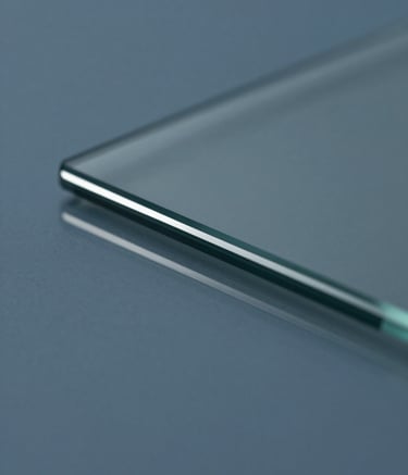 Macro shot of a clean glass surface reflecting a muted slate blue studio environment. Sharp focus on light reflecting off a polished edge, symbolizing clarity and precision. Sophisticated and minimalist composition.