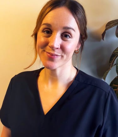 A smiling female healthcare professional wearing navy blue medical scrubs standing indoors.