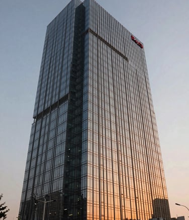 A sharp, architectural photograph of a sleek, modern glass office skyscraper in Noida during the golden hour. The building reflects a soft orange glow. The composition is a low-angle shot to emphasize height and modern aesthetics in a South Asian / Indian urban landscape.