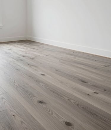 A wide-angle interior photograph of a modern North American living room featuring newly installed light grey hardwood flooring and professional white paintwork on the walls.