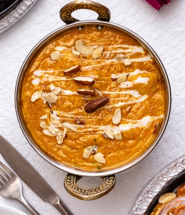 Creamy Indian butter chicken curry in a copper bowl garnished with cashews, almonds, and cream drizzle.