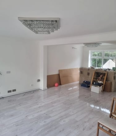 Empty living room featuring grey laminate flooring, white walls, and a modern crystal chandelier light fixture.