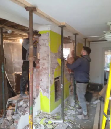 Construction workers using steel acrow props for structural support during a home wall demolition.