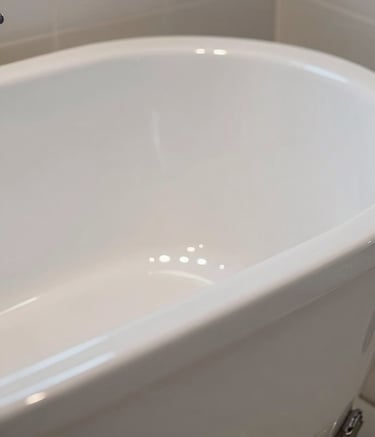 Close-up photography of a perfectly reglazed bathtub with a mirror-like high-gloss white finish. Soft lighting highlights the smooth surface and clean edges in a minimalist New York City bathroom setting.