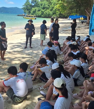 a group of students sitting on a beach during coral planting program
