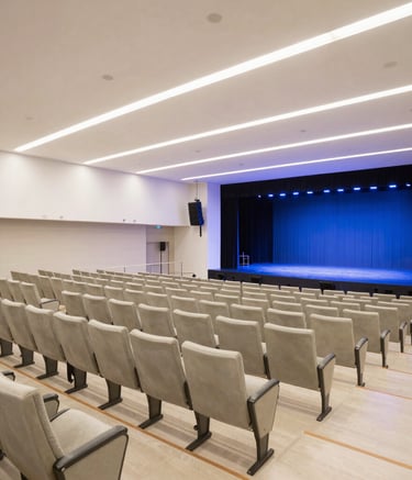 An expansive and bright interior of a modern Brazilian convention center auditorium. Rows of elegant seating lead to a stage with professional lighting. The color palette is dominated by off-white and deep blue tones, conveying a sense of corporate excellence and meticulous planning.