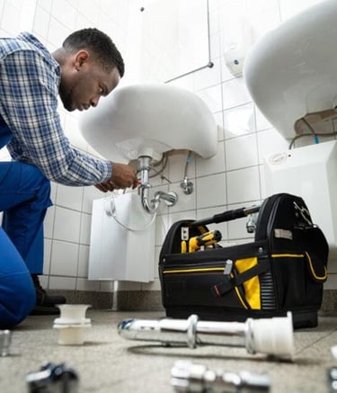 Un plombier professionnel en combinaison réparant un tuyau de lavabo dans une maison à Yaoundé