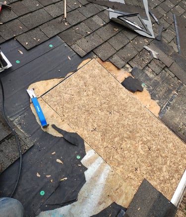 Roofing contractor replacing damaged asphalt shingles and repairing wood roof decking with tools.