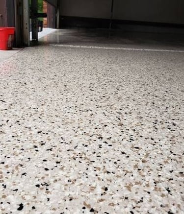 Durable epoxy garage floor coating with decorative tan and black flakes on a polished concrete surface.