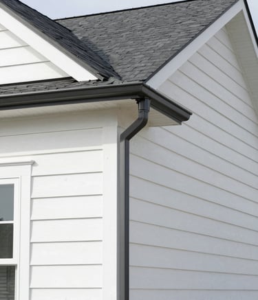 A wide-angle photography shot of a pristine North American residential home with newly installed dark slate gray gutters and soft white siding. The image is captured in bright daylight, highlighting the clean lines and durable construction.