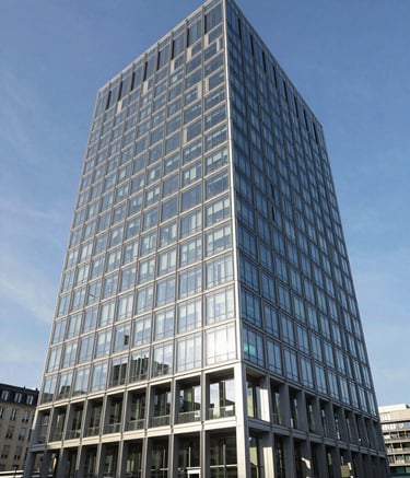 A wide-angle professional photograph of a modern glass-and-steel commercial building in a European / French city during the day. The sky is a clear Steel Blue. The architecture is clean and sophisticated, reflecting high-performance engineering. Sharp focus, bright natural lighting.