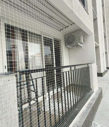 Technician carefully fitting a pigeon net on a balcony railing.