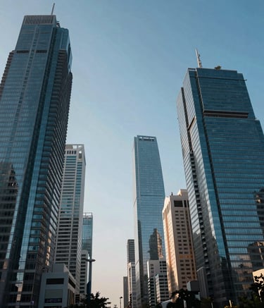 A daylight landscape photograph of a bustling financial district in an Indian metropolis. Sleek glass skyscrapers reflect the clear blue sky. The composition is wide and cinematic, conveying a sense of growth and a modern, professional economic environment.