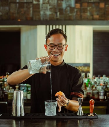 A smiling bartender pouring a clear cocktail into a crystal glass at a luxury bar.