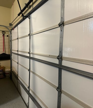 Interior view of an insulated sectional white garage door with metal hinges and tracks.