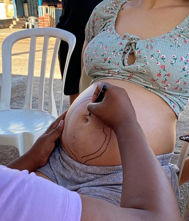 Artist drawing a creative design with a marker on a pregnant woman's belly outdoors.