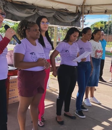 A group of women in purple shirts presenting at a community health event about maternal care.